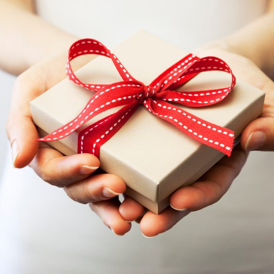 A person holding a gift box.
A woman holding a small gift box in a gesture of giving. Christmas holiday or special occasion gift box with red ribbon.